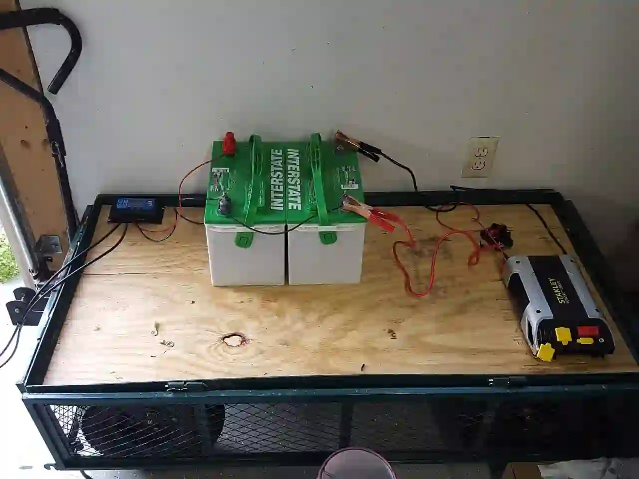 Two batteries and a battery charger inside an open storage enclosure.